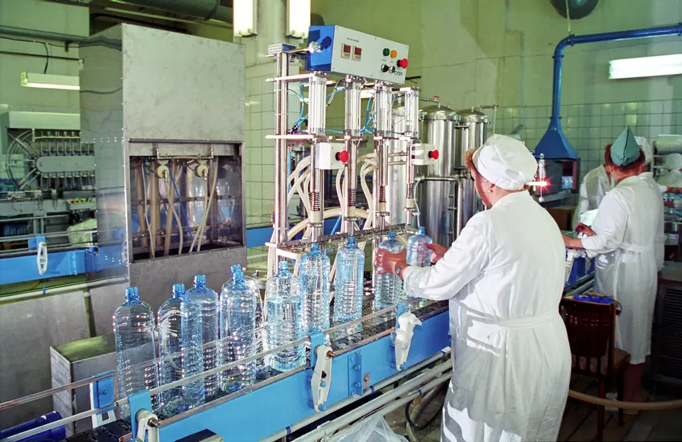Workers in white coats filling large drinking water bottles on a bottling line
