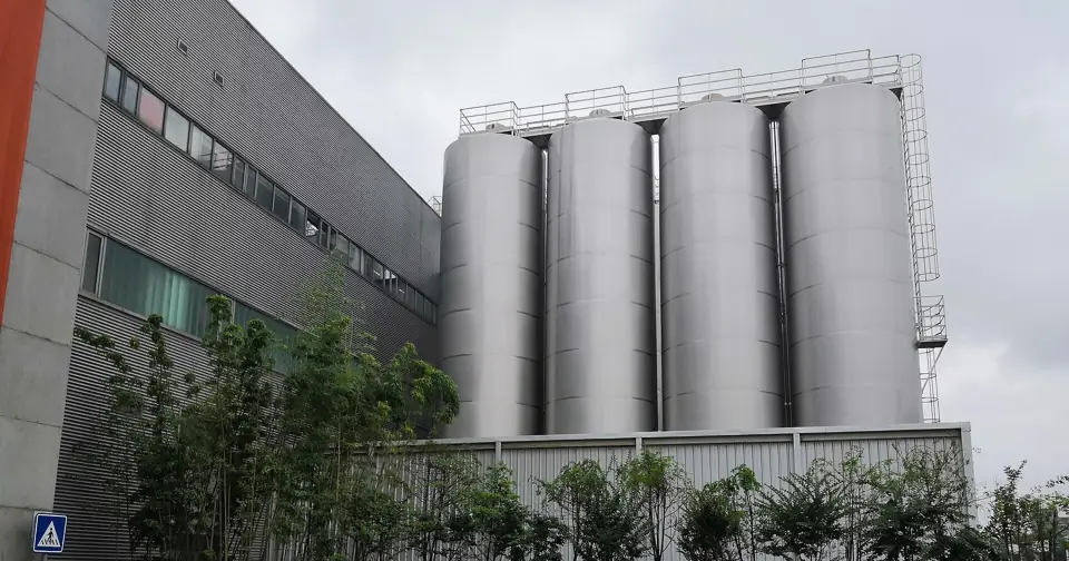 Four large stainless steel milk storage tanks outside a dairy plant